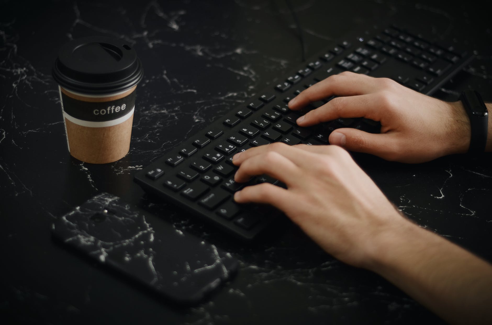 person using keyboard beside phone and coffee cup